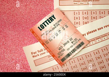 Billet de loterie rouge se trouve sur des feuilles de jeu roses avec des numéros pour marquer pour jouer à la loterie. Concept de jeu de loterie ou dépendance au jeu. Gros plan Banque D'Images