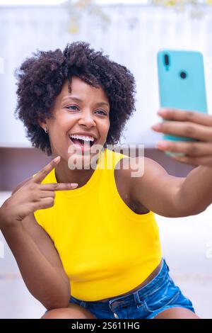 Jeune femme afro-américaine excitée prenant un Selfie avec un smartphone à l'extérieur Banque D'Images