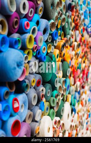 Un tableau de bobines colorées et vibrantes de fil empilées soigneusement dans un affichage de magasin de textile Banque D'Images