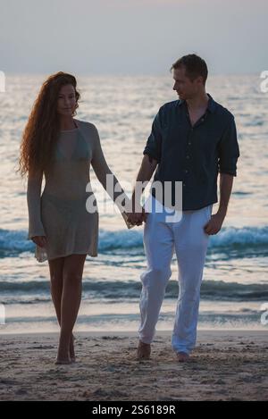 Couple marchant sur une plage de sable au coucher du soleil en Thaïlande Banque D'Images
