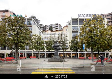 Lugano, Suisse - 22 décembre 2024 : Piazza Carlo Battaglini avec sa statue emblématique et ses bancs rouges Banque D'Images