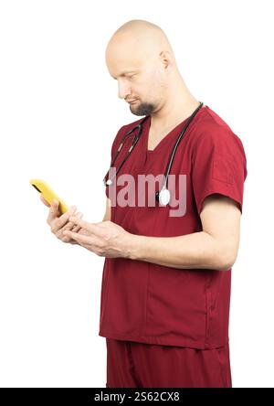 Un médecin chauve portant des gommages médicaux rouges et un stéthoscope autour du cou regarde un smartphone jaune. Banque D'Images