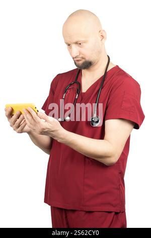 Un médecin chauve portant des gommages rouges et un stéthoscope tient un smartphone jaune. Banque D'Images