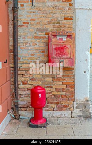 Venise, Italie - 10 janvier 2017 : boîte postale italienne au mur de briques et borne d'incendie rouge dans l'île de Burano voyage d'hiver. Banque D'Images