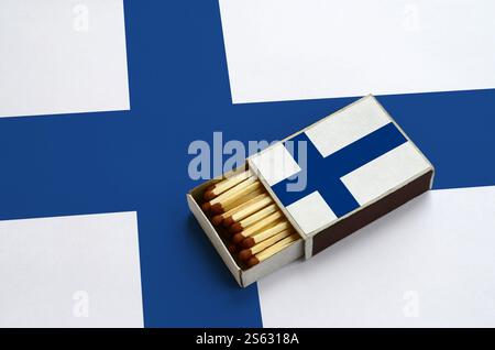 Le drapeau de la Finlande est représenté dans une boîte d'allumettes ouverte, remplie d'allumettes et reposant sur un grand drapeau. Le drapeau de la Finlande est affiché dans une boîte d'allumettes ouverte, qui est Banque D'Images