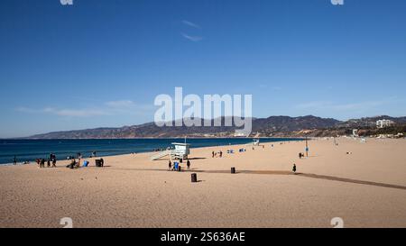 Les gens se détendent et participent à diverses activités sur la plage de Santa Monica sous un ciel bleu clair. La tour des sauveteurs surplombe la rive sablonneuse Banque D'Images