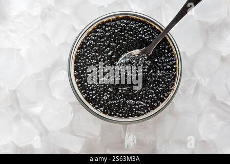 Caviar d'esturgeon noir dans un bocal en verre sur glace, vue de dessus. Caviar d'esturgeon ou de béluga sur cuillère. Banque D'Images