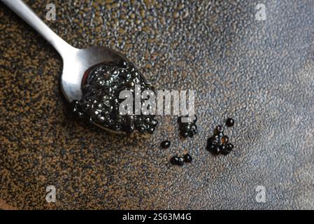 Caviar d'esturgeon noir sur cuillère sur fond brun foncé gros plan, espace de copie. Esturgeon sauvage ou caviar de béluga. Banque D'Images