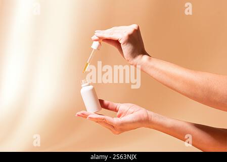 Les mains de la femme tiennent compte-gouttes de sérum sur fond beige avec des ombres, espace de copie. Sérum anti-âge rétinol en flacon blanc, produit cosmétique de marque. Dail Banque D'Images