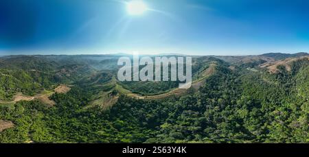 Vue aérienne d'Une vue aérienne à couper le souffle d'une chaîne de montagnes luxuriante et verte sous un ciel bleu clair et lumineux, avec la lumière du soleil illuminant le vaste, vallonné Banque D'Images