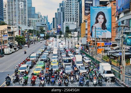 Une vue depuis Asoke intersection sur Asok Montri Road, une artère majeure de Bangkok, avec des gratte-ciel, de grands panneaux d'affichage et de nombreuses voitures et motos Banque D'Images