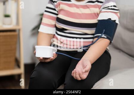 Femme en surpoids plus taille auto-contrôles mesurant la pression artérielle et l'auto-contrôle du tonomètre de fréquence cardiaque à la maison. Banque D'Images