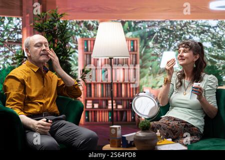 Les personnes âgées appliquant le sérum rajeunissant et faisant la routine quotidienne ensemble pour les soins de la peau, afin de préserver leur peau vieillissante. Couple utilisant un hydratant et une crème de protection UV sur leurs joues. Banque D'Images