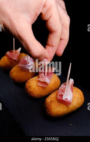 Main ramasser une croquette avec du jambon serrano Banque D'Images
