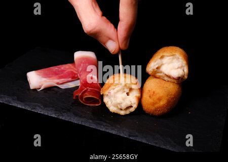 Cueillette à la main une croquette de jambon avec des tranches de jambon séché sur une assiette d'ardoise Banque D'Images