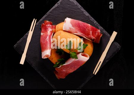 Délicieux jambon et croquettes avec fourchettes en bois sur assiette en ardoise Banque D'Images