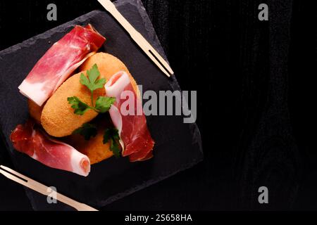 Croquettes et jambon avec fourchettes en bois sur plaque carrée en ardoise avec espace négatif à droite Banque D'Images