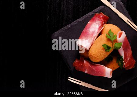 Croquettes et jambon avec fourchettes en bois sur plaque carrée en ardoise avec espace négatif à gauche Banque D'Images