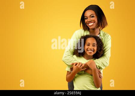 L'amour de la mère. Bonne maman afro-américaine affectueuse qui câlin sa fille du dos, debout sur fond jaune Banque D'Images