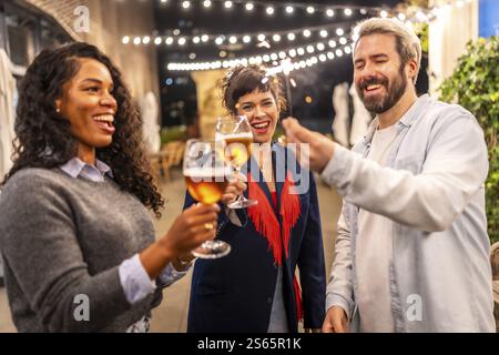 Amis multiethniques toast avec de la bière et tenant des pétillants tout en profitant d'une soirée Banque D'Images
