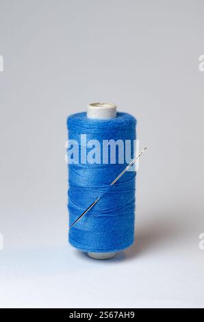 Une bobine de fil bleu simple avec aiguille sur fond blanc Banque D'Images