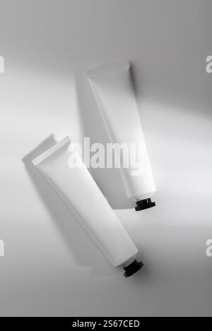 Composition minimaliste de deux tubes cosmétiques blancs avec des capuchons noirs sur une surface lumineuse avec des ombres douces. Idéal pour la marque, la conception de produits et SK Banque D'Images