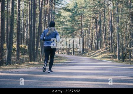 Une femme en vêtements de sport court le long d'un chemin forestier. Banque D'Images