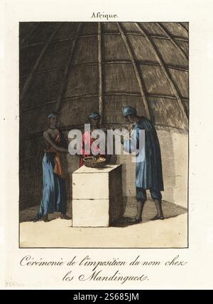 Cérémonie de remise du nom du peuple mandingue, Afrique de l'Ouest, XVIIIe siècle. Dans une cabane en bois à dôme, un maître d'école ou un prêtre prie sur un bol calabash de dega (maïs et lait aigre), avant de tenir le bébé, cracher trois fois au visage et le nommer. Les assistants partagent ensuite le dega avec leur main droite. Ceremonie de l'imposition du nom chez les Mandingue. Gravure sur cuivre colorée à la main tirée de Moeurs et Coutumes des peuples ou Collection de tableaux représentant les usages remarquables, les mariages, funérailles, supplices et fêtes des diverses Nations du monde, Manners and Customs of PEO Banque D'Images