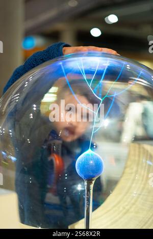 Jeune garçon touchant le globe plasma, expérimentant les merveilles de l'électricité statique dans une exposition interactive du musée des sciences Banque D'Images