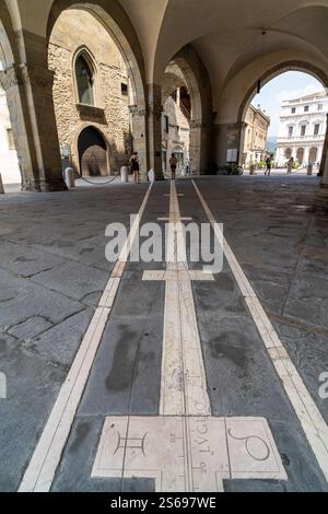 Une vue détaillée d'un cadran solaire en pierre historique encastré dans le sol, situé sous un portique magnifiquement arqué dans une charmante ville italienne. Banque D'Images