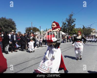 Une jeune mère avec sa fille dans les bras toutes deux vêtues de costumes crétois traditionnels participe au défilé de la fête nationale grecque Banque D'Images