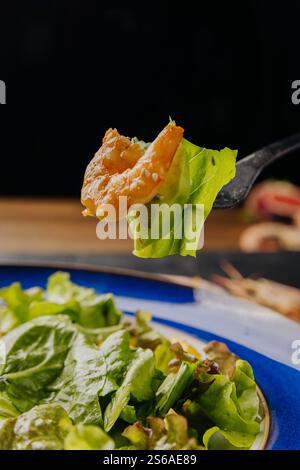 Gros plan d'une fourchette tenant une crevette et une laitue sur une assiette à salade fraîche et vibrante Banque D'Images