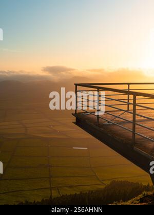 Une vue imprenable sur le coucher du soleil depuis une terrasse d'observation surplombant de vastes champs verdoyants et des collines ondulantes, dans une lumière dorée. Terceira, Açores, Portugal Banque D'Images