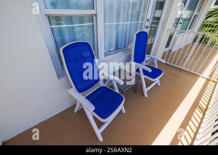 Deux chaises longues bleues avec cadres blancs et petite table grise sur le balcon de l'hôtel avec vue sur les palmiers. Miami Beach. ÉTATS-UNIS. Banque D'Images
