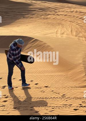 Homme âgé marchant avec un plateau de sable sous le bras vers le haut dune de sable Banque D'Images