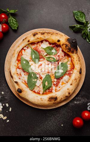 Délicieuse pizza gastronomique avec épinards, amandes et tomates fraîches sur une assiette en bois Banque D'Images