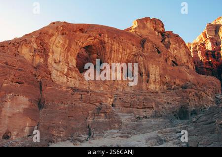 Une montagne rocheuse avec un grand trou au milieu. Le trou est entouré de rochers et il est une grotte. La montagne est couverte d'une couleur brun rougeâtre, Banque D'Images