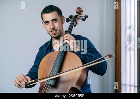 Jeune musicien jouant du violoncelle à l'intérieur avec arc et cordes. Banque D'Images