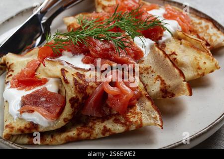 Délicieuses crêpes au saumon et à la crème sure, petit déjeuner, sur une assiette, style rustique, avec couverts Banque D'Images