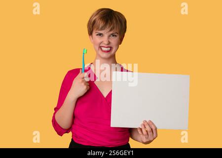 Une jeune femme avec un sourire blanc neige tient une brosse à dents et une feuille blanche pour écrire du texte dessus. Banque D'Images