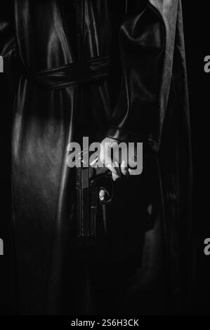 La silhouette d'une détective dans un manteau avec un pistolet dans les mains, qu'elle cache derrière son dos. instantané noir et blanc. Banque D'Images