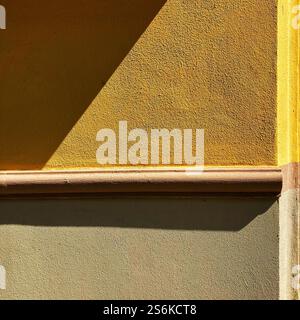 Composition minimaliste mettant en valeur un mur ensoleillé avec des teintes jaunes et beiges vibrantes, mettant en valeur les formes géométriques et les surfaces texturées Banque D'Images