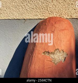 Vue rapprochée d'une borne en pierre vieillie devant un mur texturé, présentant des textures et des détails éclairés par la lumière du soleil Banque D'Images