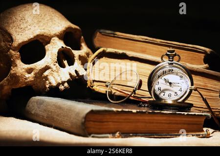 Vieilles lunettes en gros plan sur le livre près du crâne humain et montre de poche Banque D'Images