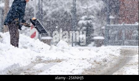 Un homme pelle la neige de la route. La neige est entassée sur le sol et l'homme utilise un chasse-neige pour déneiger. La scène est froide et sno Banque D'Images