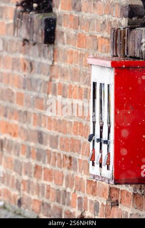 Un distributeur automatique rouge avec trois compartiments se trouve sur un mur de briques. La machine est recouverte de neige, ce qui lui donne un aspect quelque peu abandonné et négligé Banque D'Images