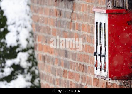 Un distributeur automatique rouge à trois compartiments est recouvert de neige. La neige tombe sur le bâtiment et la machine, créant un cadre paisible et serein Banque D'Images