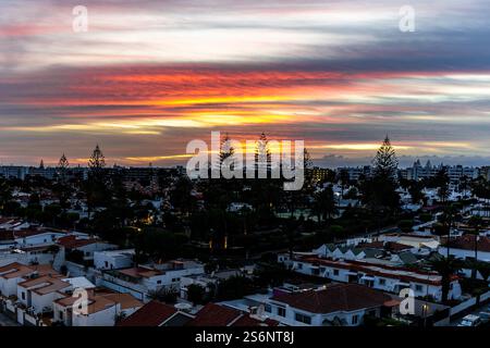 Un beau coucher de soleil sur un paysage urbain avec des maisons et des palmiers. Le ciel est rempli de nuages et le soleil se couche, créant un guichet automatique chaud et paisible Banque D'Images