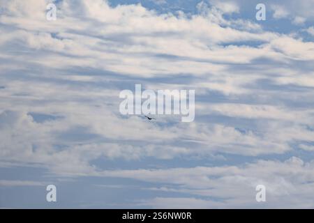 Un hélicoptère vole à travers un ciel nuageux. Le ciel est principalement bleu avec quelques nuages blancs dispersés partout Banque D'Images