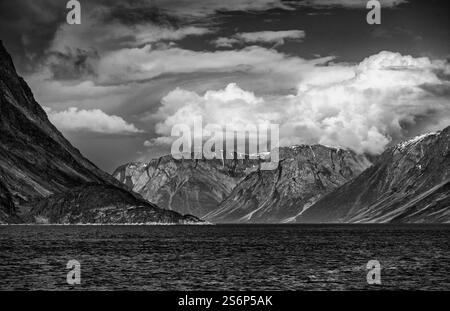 Le fjord de Kangerlussuaq au Groenland présente des montagnes imposantes et des nuages saisissants au-dessus des eaux calmes, créant un paysage naturel à couper le souffle. Banque D'Images